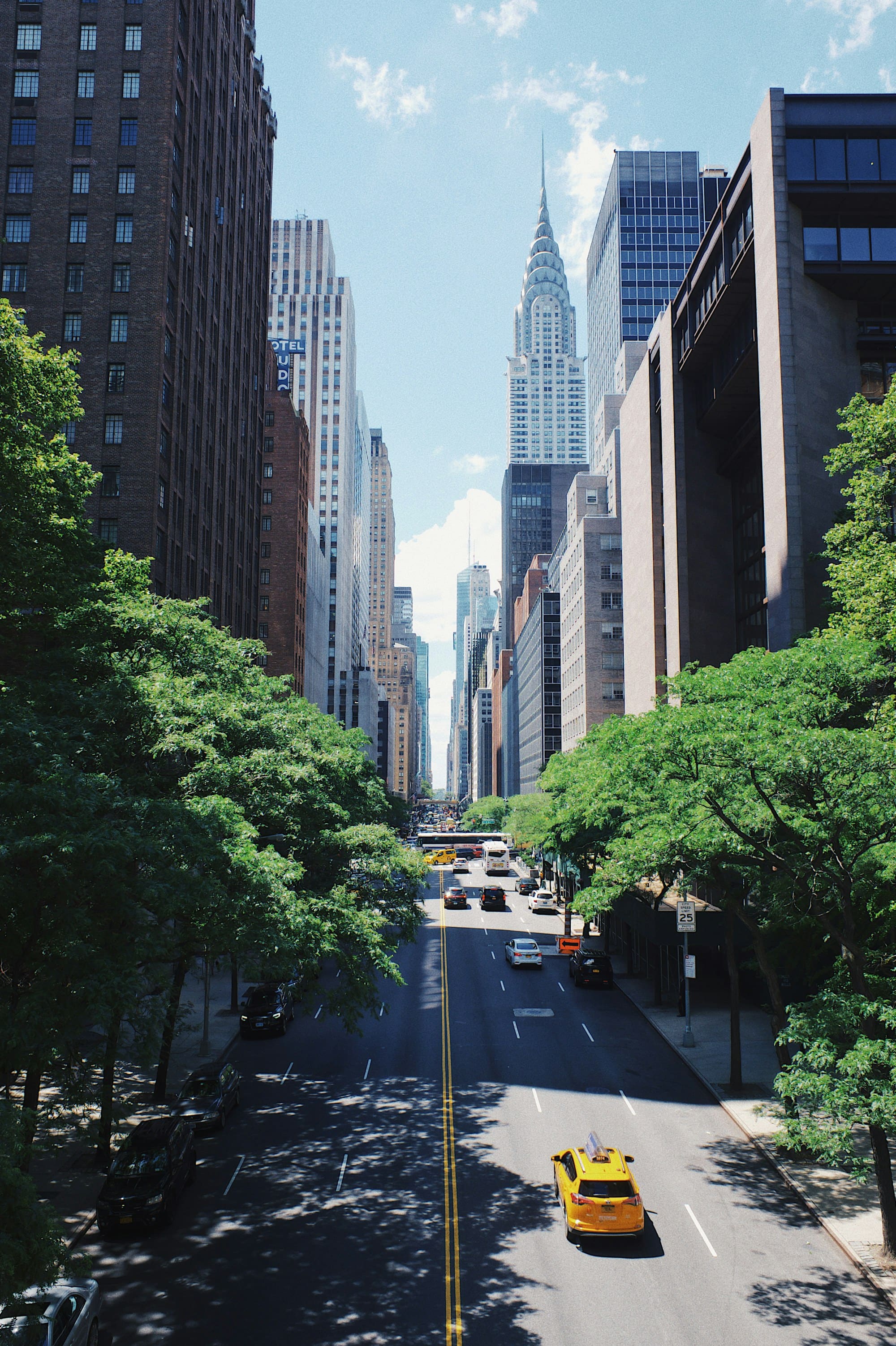 A sunlit Manhattan avenue with a yellow cab and the Chrysler Building beyond