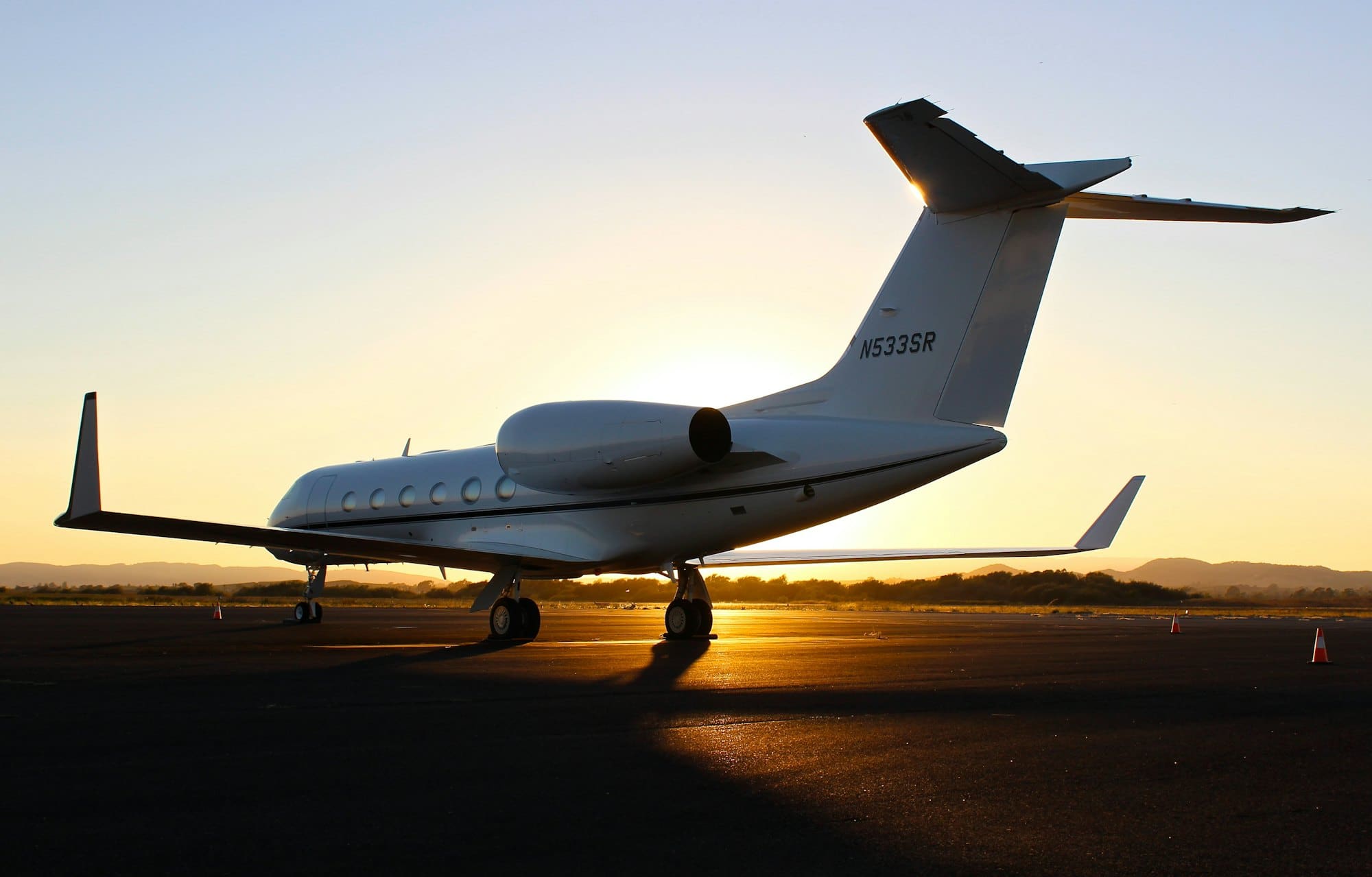 A private jet on the tarmac at golden hour, silhouetted against the low sun